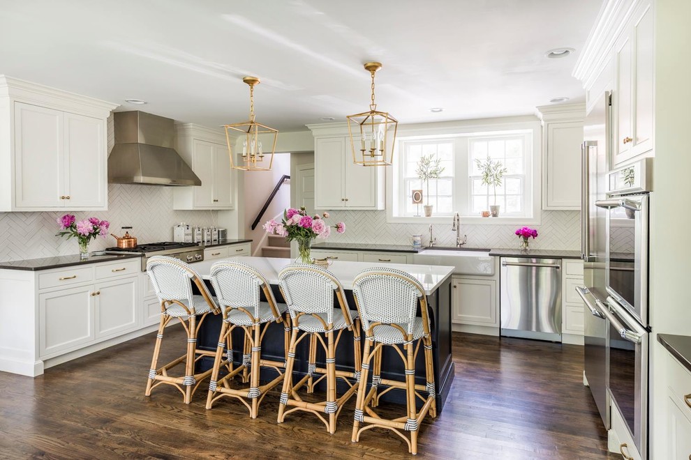 This is an example of a traditional kitchen in New York with a farmhouse sink, shaker cabinets, white cabinets, white splashback, stainless steel appliances, dark hardwood floors, with island and brown floor.