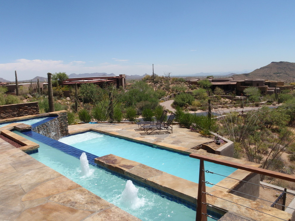 Example of a large backyard custom-shaped infinity pool fountain design in Phoenix with decking