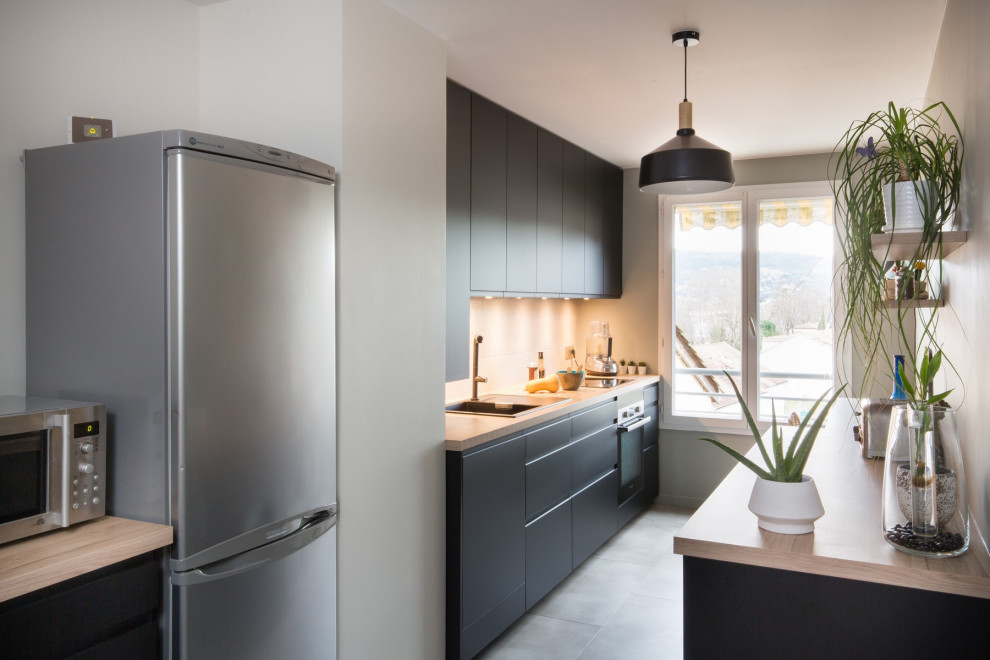 Contemporary galley kitchen in Lille with a drop-in sink, flat-panel cabinets, black cabinets, wood benchtops, stainless steel appliances, no island, grey floor and beige benchtop.