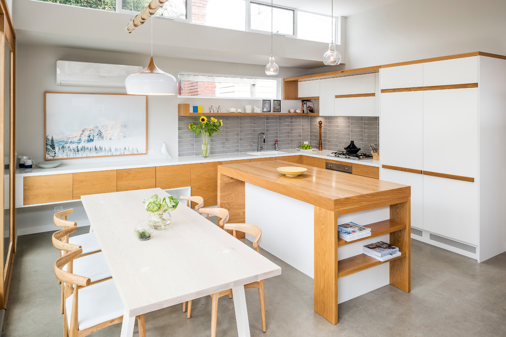 Inspiration for a contemporary l-shaped eat-in kitchen in Melbourne with flat-panel cabinets, grey splashback, panelled appliances, concrete floors and with island.