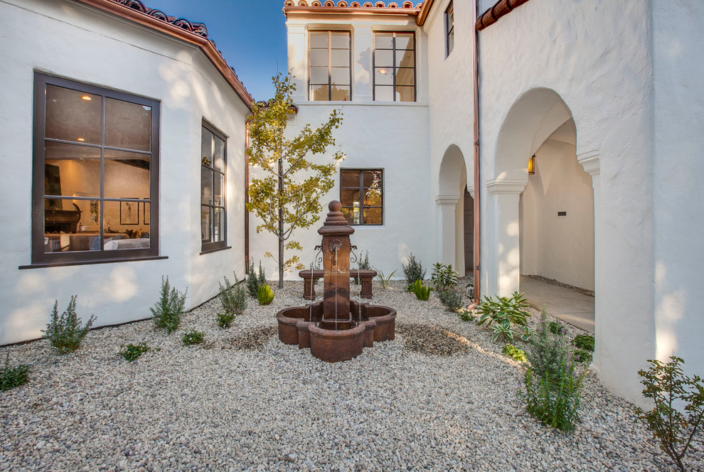 Photo of a mid-sized mediterranean courtyard formal garden in Los Angeles with a water feature and gravel.
