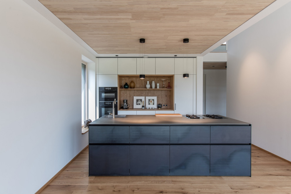 Inspiration for a contemporary galley kitchen in Munich with an integrated sink, flat-panel cabinets, white cabinets, brown splashback, timber splashback, black appliances, medium hardwood floors, with island, brown floor and grey benchtop.