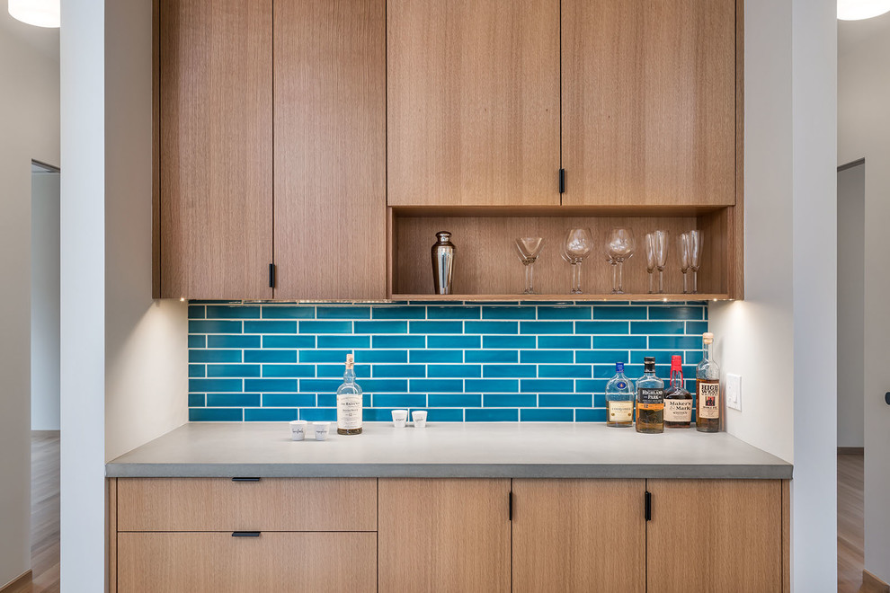 Small modern galley home bar in Portland with flat-panel cabinets, light wood cabinets, concrete benchtops, blue splashback, ceramic splashback, light hardwood floors, grey benchtop and an undermount sink.