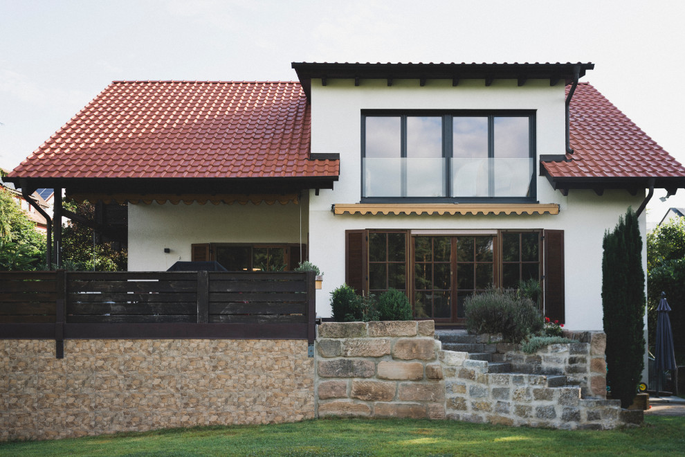 На фото: маленький, одноэтажный, белый частный загородный дом в современном стиле с облицовкой из цементной штукатурки, двускатной крышей, черепичной крышей и красной крышей для на участке и в саду