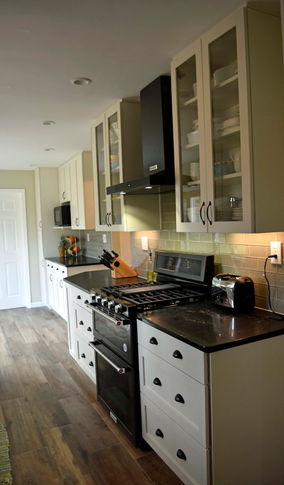 Inspiration for a mid-sized transitional galley laminate floor and brown floor enclosed kitchen remodel in DC Metro with a farmhouse sink, shaker cabinets, white cabinets, granite countertops, gray backsplash, subway tile backsplash, stainless steel appliances, no island and black countertops