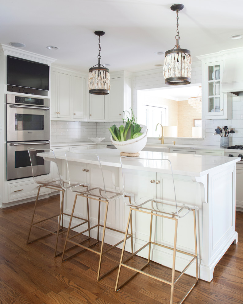 Inspiration for a transitional l-shaped kitchen in Charlotte with shaker cabinets, white cabinets, white splashback, subway tile splashback, stainless steel appliances, medium hardwood floors, with island and brown floor.