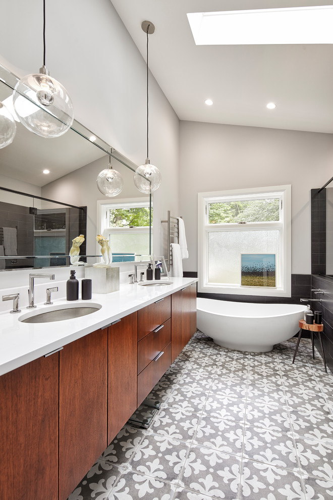 Inspiration for a contemporary master bathroom in Other with flat-panel cabinets, dark wood cabinets, a freestanding tub, black tile, grey walls, an undermount sink and grey floor.