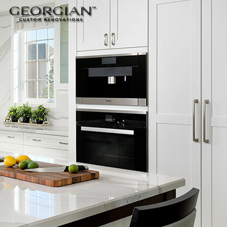 Small transitional l-shaped medium tone wood floor kitchen photo with an undermount sink, shaker cabinets, white cabinets, quartzite countertops, white backsplash, stone slab backsplash, stainless steel appliances and an island