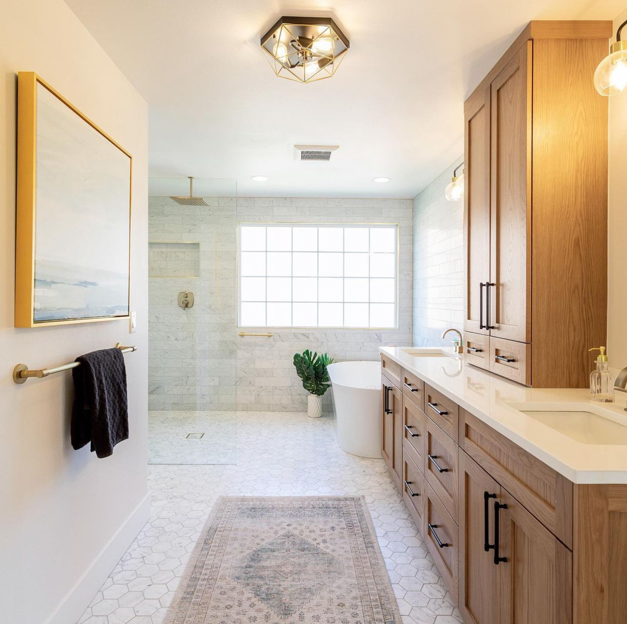 This spacious spa bath blends traditional charm with modern updates, featuring a full marble tile surround, hex mosaic flooring, and a freestanding soaking tub with brushed gold hardware. LuxeRevive d