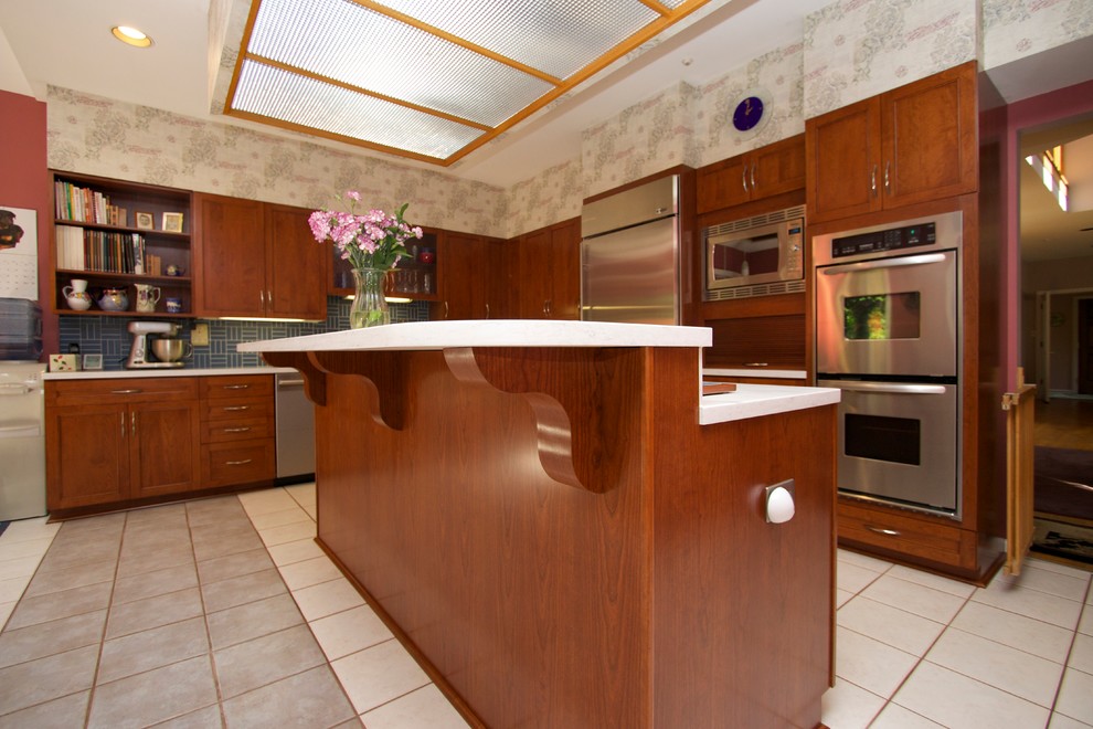 Inspiration for a transitional l-shaped ceramic tile open concept kitchen remodel in Baltimore with an undermount sink, recessed-panel cabinets, medium tone wood cabinets, solid surface countertops, blue backsplash, ceramic backsplash, stainless steel appliances and an island