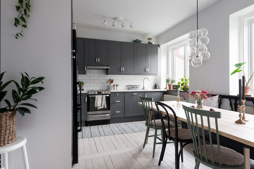 Inspiration for a mid-sized scandinavian l-shaped open plan kitchen in Gothenburg with a drop-in sink, beaded inset cabinets, grey cabinets, laminate benchtops, white splashback, ceramic splashback, black appliances, light hardwood floors, no island and white floor.