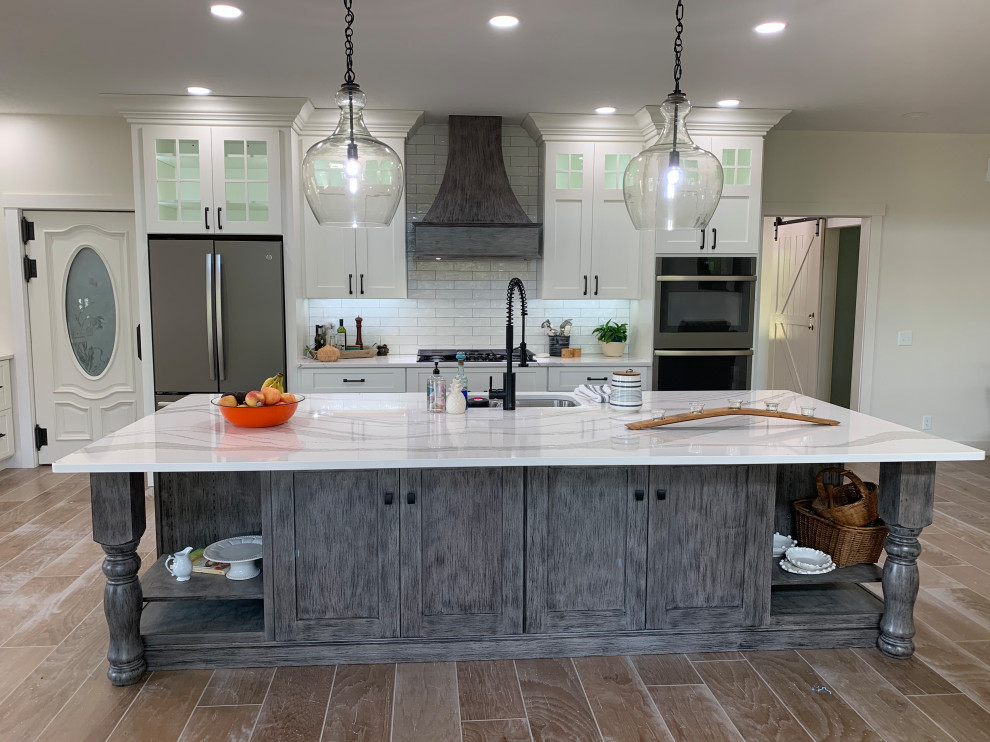 Inspiration for a large rustic l-shaped open plan kitchen in Other with a submerged sink, recessed-panel cabinets, white cabinets, engineered stone countertops, white splashback, stainless steel appliances, an island, brown floors and white worktops.