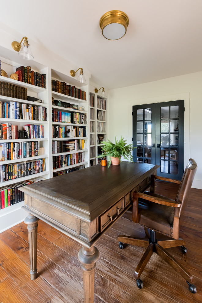 Photo of a large country home office in Nashville with a library, white walls, medium hardwood floors, a freestanding desk and brown floor.