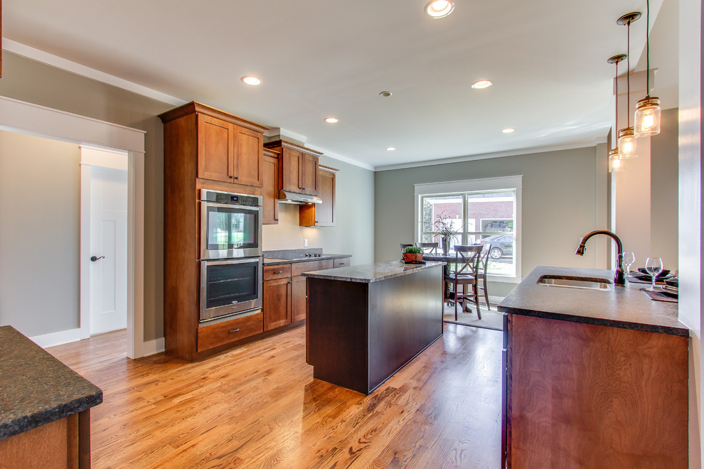 Inspiration for a large arts and crafts u-shaped open plan kitchen in Nashville with an undermount sink, flat-panel cabinets, medium wood cabinets, granite benchtops, stainless steel appliances, medium hardwood floors and multiple islands.