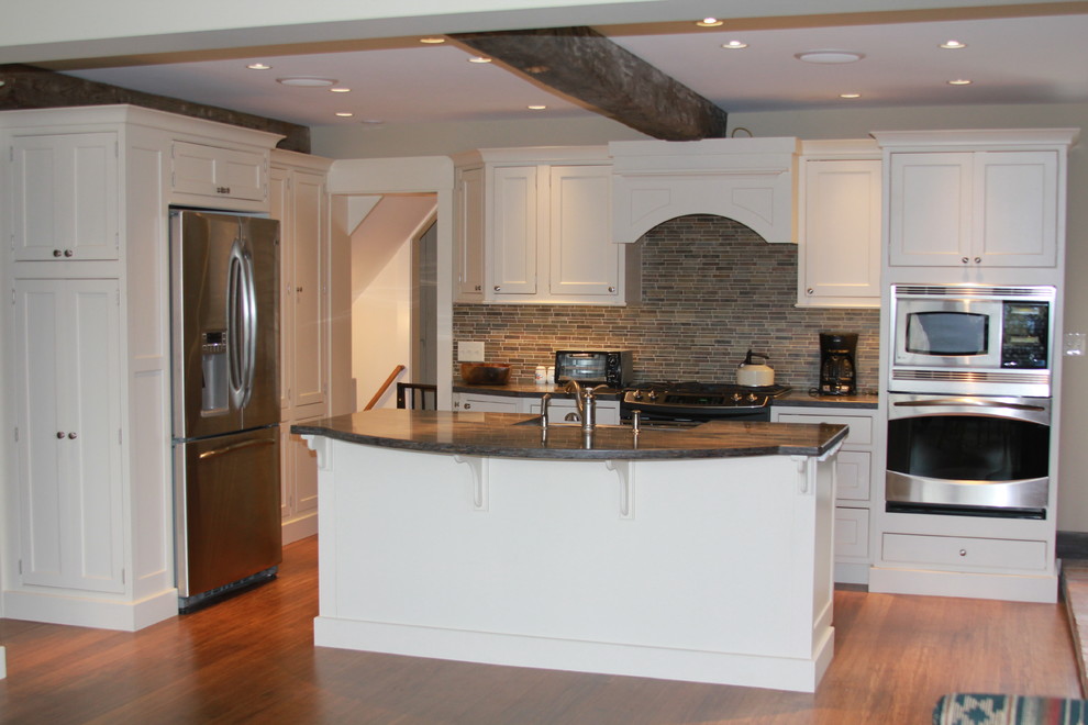 Inspiration for a large traditional l-shaped open plan kitchen in Boston with a farmhouse sink, beaded inset cabinets, white cabinets, solid surface benchtops, stainless steel appliances, with island and grey splashback.