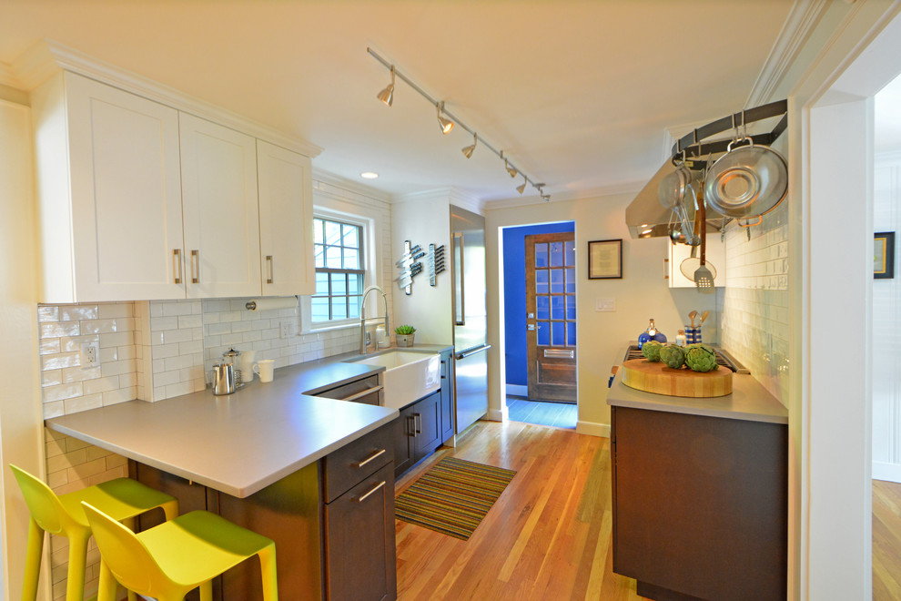Enclosed kitchen - small transitional galley light wood floor enclosed kitchen idea in Boston with a farmhouse sink, flat-panel cabinets, dark wood cabinets, quartz countertops, white backsplash, subway tile backsplash, stainless steel appliances and a peninsula