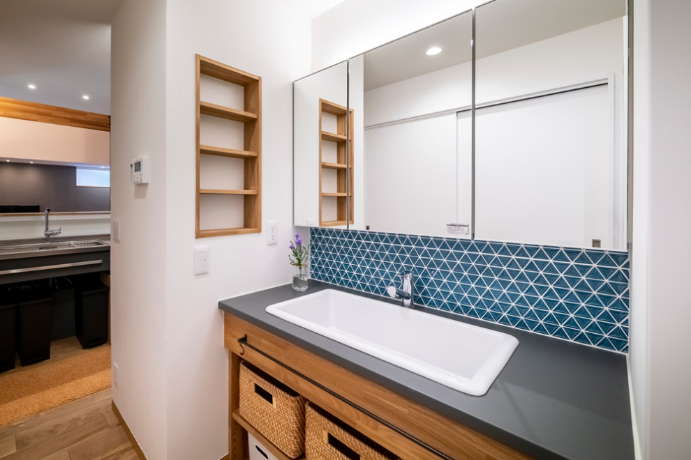 Aménagement d'un WC et toilettes contemporain de taille moyenne avec un placard sans porte, des portes de placard blanches, un carrelage bleu, mosaïque, un mur blanc, un sol en bois brun, un lavabo posé, un sol beige, un plan de toilette gris et meuble-lavabo encastré.