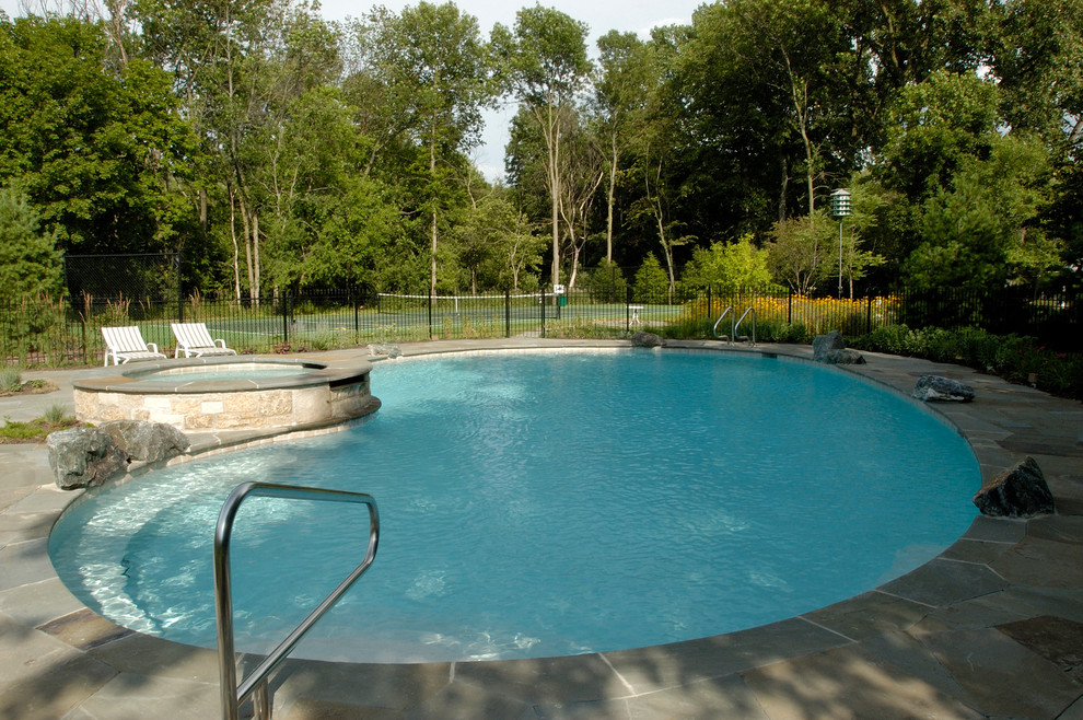 This is an example of a large country backyard custom-shaped natural pool in Chicago with a hot tub and natural stone pavers.