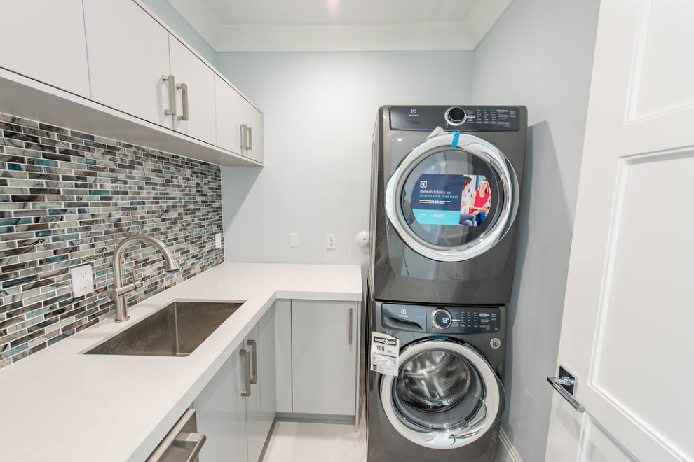 Contemporary l-shaped laundry room in Miami with an undermount sink, blue cabinets, quartz benchtops, blue splashback, mosaic tile splashback, blue walls, ceramic floors, a stacked washer and dryer and white benchtop.
