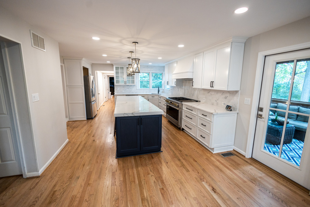 Inspiration for a large transitional l-shaped light wood floor and brown floor eat-in kitchen remodel in Baltimore with an undermount sink, shaker cabinets, white cabinets, quartz countertops, white backsplash, marble backsplash, stainless steel appliances, an island and white countertops