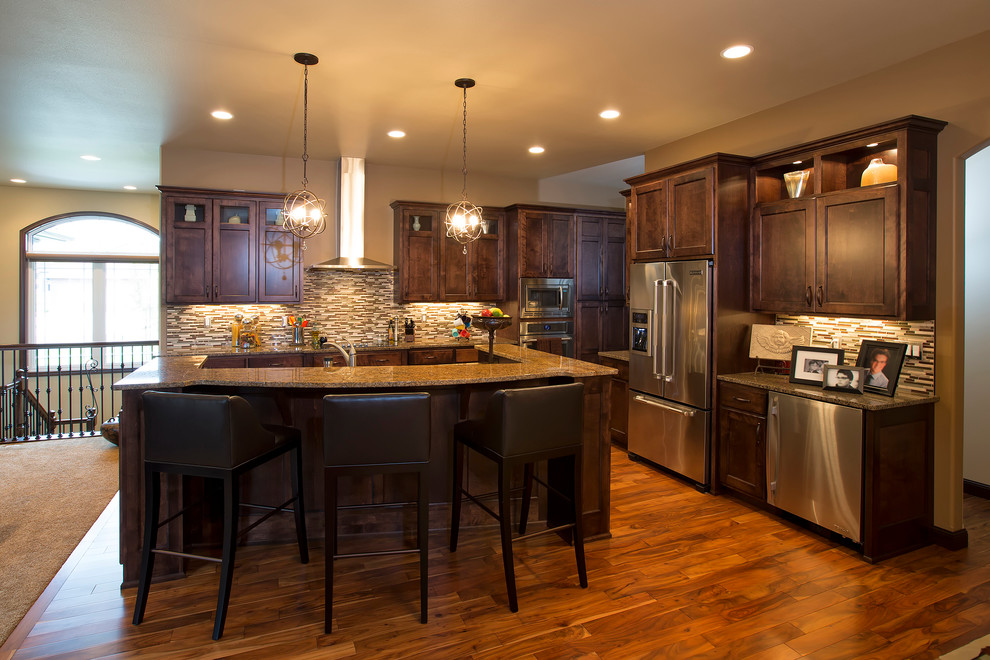 Example of a transitional l-shaped medium tone wood floor open concept kitchen design with an undermount sink, recessed-panel cabinets, dark wood cabinets, granite countertops, multicolored backsplash, mosaic tile backsplash, stainless steel appliances and an island