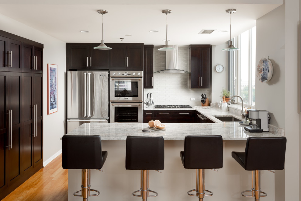 Mid-sized transitional u-shaped open plan kitchen in Chicago with an undermount sink, shaker cabinets, dark wood cabinets, white splashback, stainless steel appliances, medium hardwood floors, marble benchtops, subway tile splashback and no island.