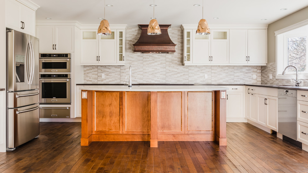 Example of a mid-sized transitional u-shaped medium tone wood floor eat-in kitchen design in Calgary with an undermount sink, recessed-panel cabinets, white cabinets, quartz countertops, gray backsplash, ceramic backsplash, stainless steel appliances and an island