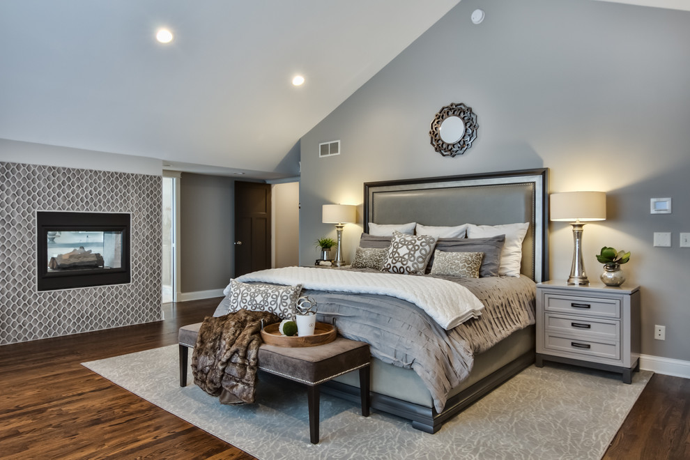 Design ideas for a transitional master bedroom in Minneapolis with grey walls, a two-sided fireplace, a tile fireplace surround and brown floor.