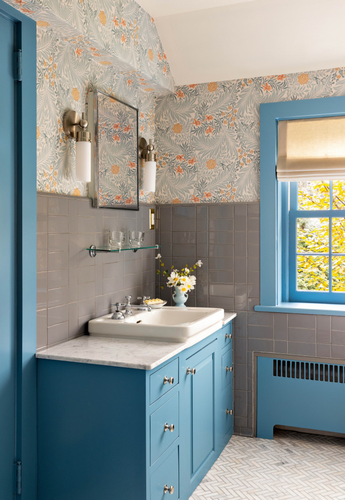 Mid-sized country 3/4 bathroom in New York with blue cabinets, gray tile, ceramic tile, marble floors, marble benchtops, a single vanity, a built-in vanity, wallpaper, raised-panel cabinets, multi-coloured walls, a drop-in sink, white floor and white benchtops.