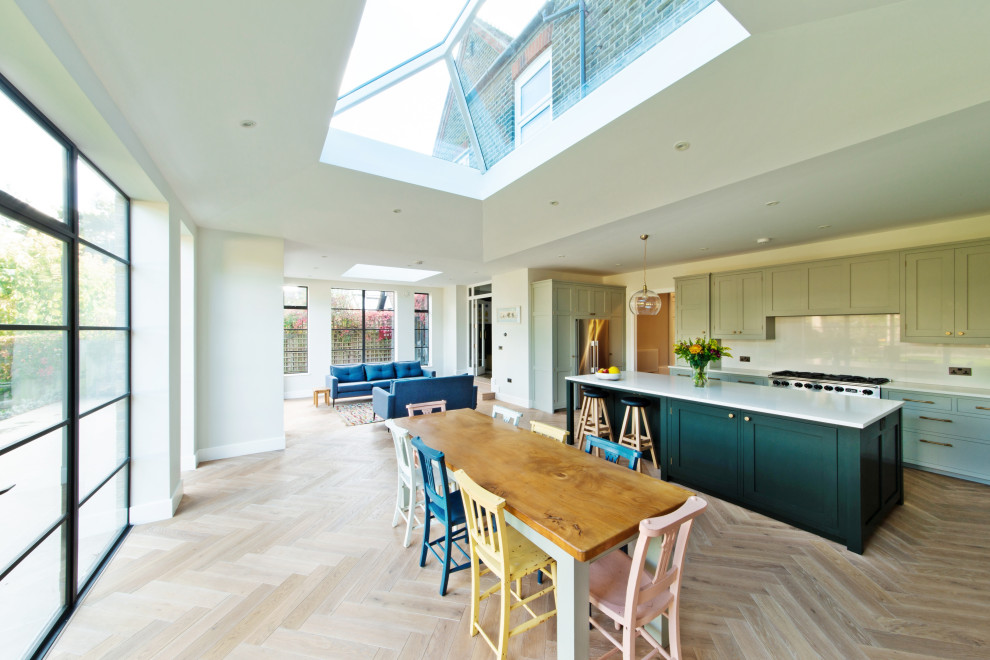 This is an example of a large transitional u-shaped open plan kitchen in London with an undermount sink, shaker cabinets, green cabinets, quartzite benchtops, white splashback, engineered quartz splashback, stainless steel appliances, medium hardwood floors, with island and white benchtop.
