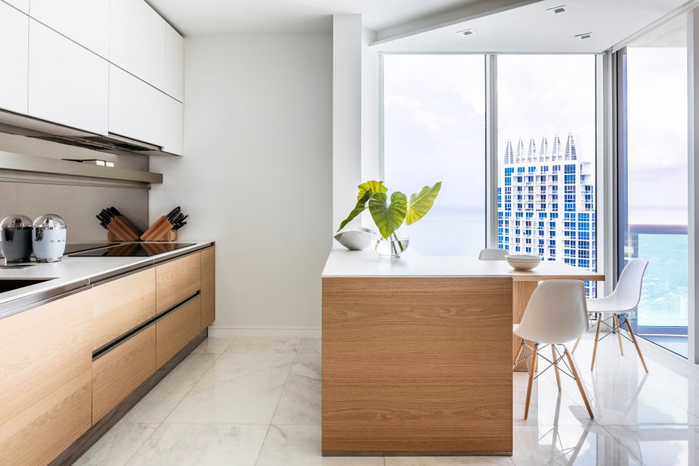 This is an example of a contemporary galley eat-in kitchen in Miami with an undermount sink, flat-panel cabinets, medium wood cabinets, a peninsula, white floor and white benchtop.