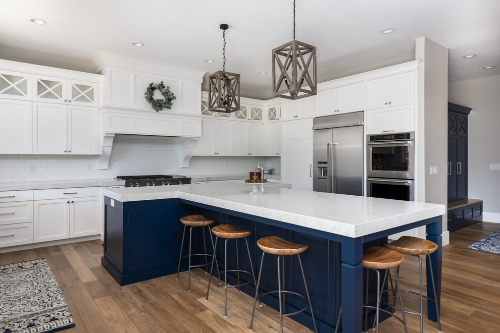 This is an example of a transitional kitchen in Salt Lake City with shaker cabinets, white cabinets, white splashback, subway tile splashback, stainless steel appliances, medium hardwood floors, with island and white benchtop.