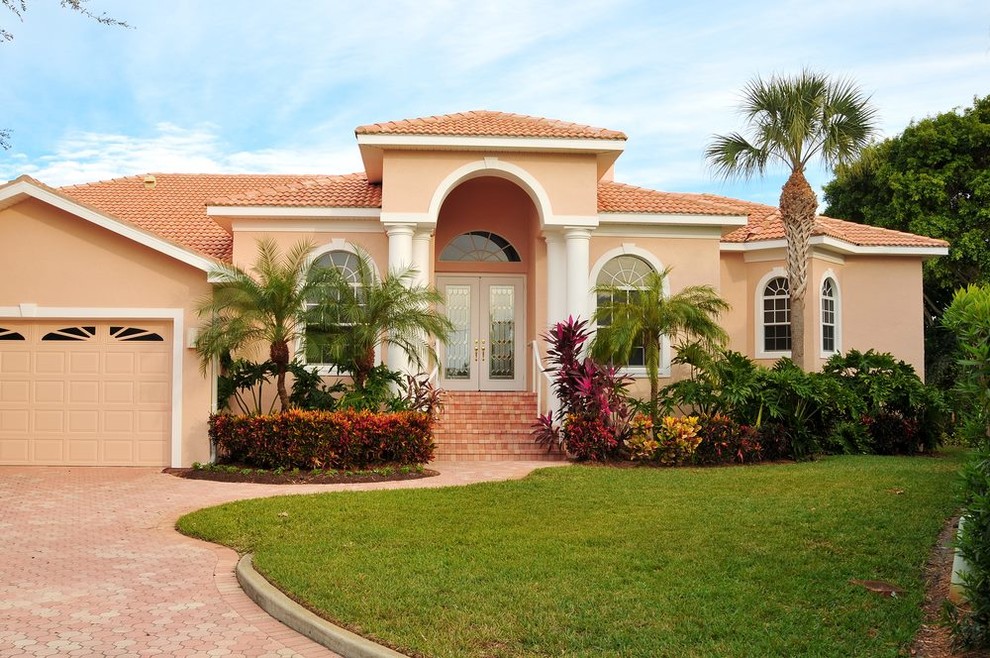 Photo of a large traditional two-storey stucco orange house exterior in Tampa with a gable roof and a tile roof.