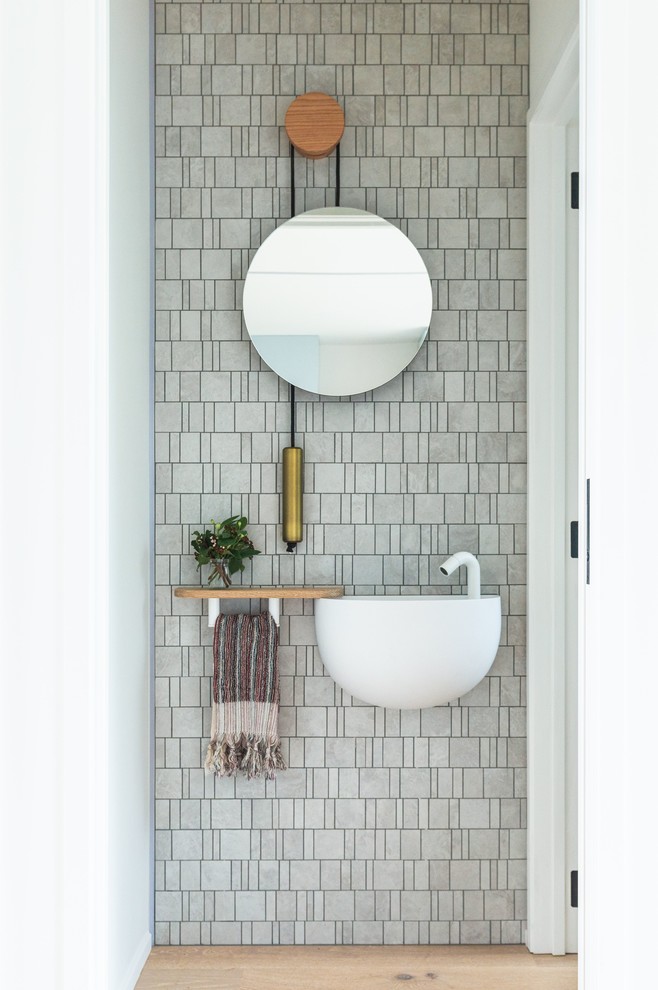 Photo of a contemporary powder room in Hamilton with gray tile, mosaic tile, white walls, medium hardwood floors, a wall-mount sink and brown floor.