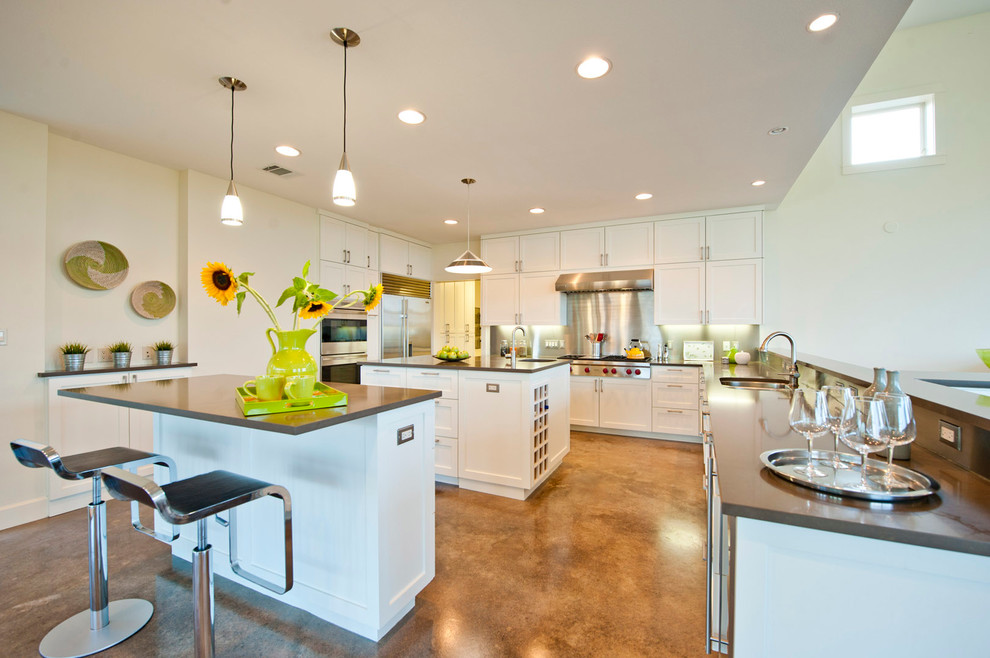 This is an example of a large contemporary u-shaped kitchen pantry in Austin with an undermount sink, recessed-panel cabinets, white cabinets, quartz benchtops, metallic splashback, metal splashback, stainless steel appliances, concrete floors and multiple islands.