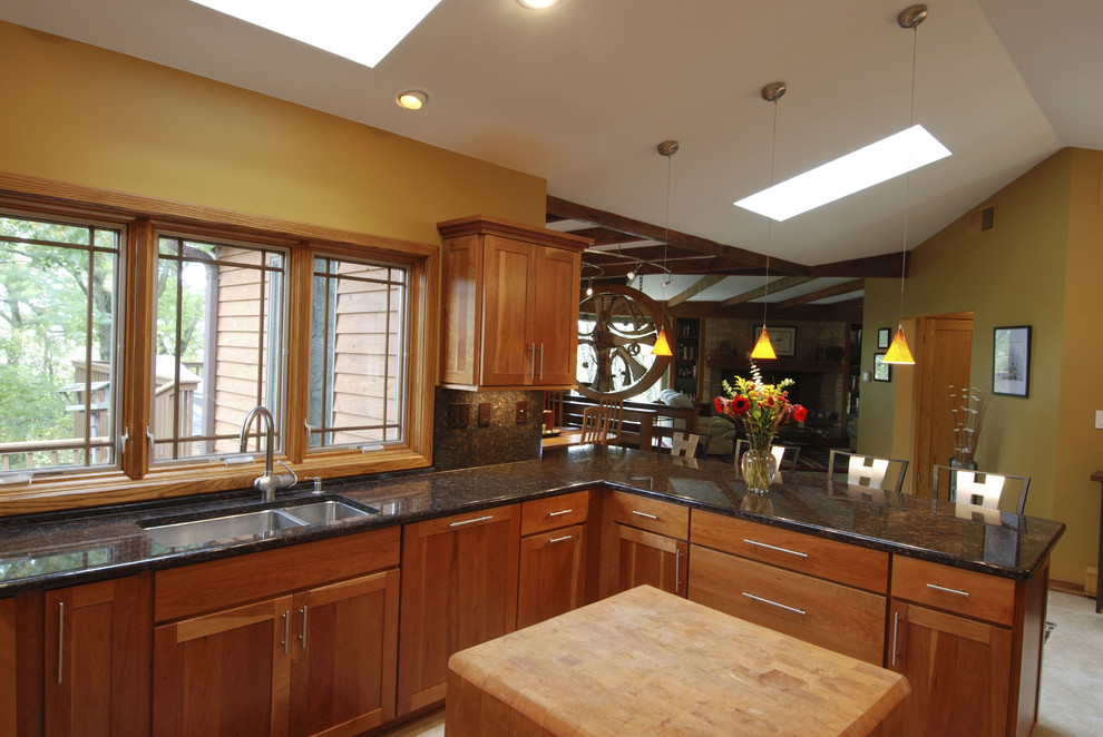 This is an example of a transitional u-shaped eat-in kitchen in Milwaukee with an undermount sink, recessed-panel cabinets, medium wood cabinets, granite benchtops, brown splashback, stone slab splashback and stainless steel appliances.