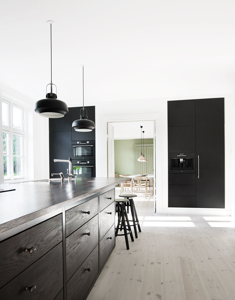 Large contemporary kitchen in Odense with flat-panel cabinets, black cabinets, light hardwood floors and with island.