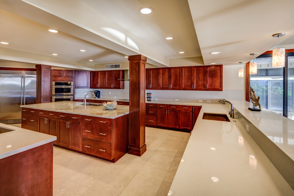 Inspiration for a large tropical open plan kitchen in Hawaii with an undermount sink, shaker cabinets, medium wood cabinets, solid surface benchtops, stainless steel appliances, limestone floors and multiple islands.