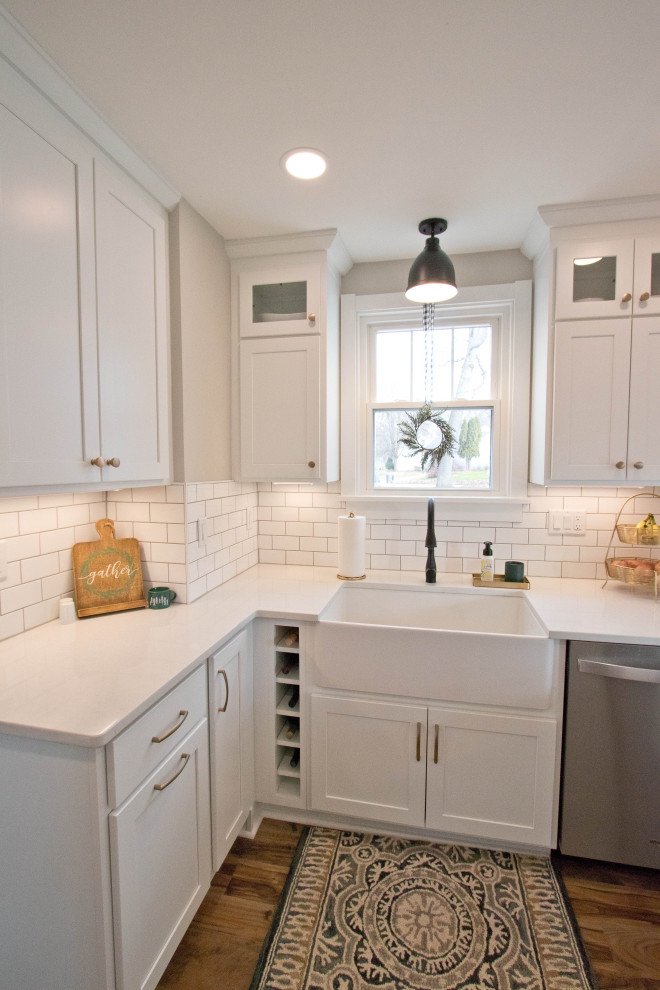 Example of a mid-sized mountain style galley vinyl floor and brown floor enclosed kitchen design with a farmhouse sink, recessed-panel cabinets, white cabinets, quartz countertops, white backsplash, subway tile backsplash, stainless steel appliances, a peninsula and white countertops