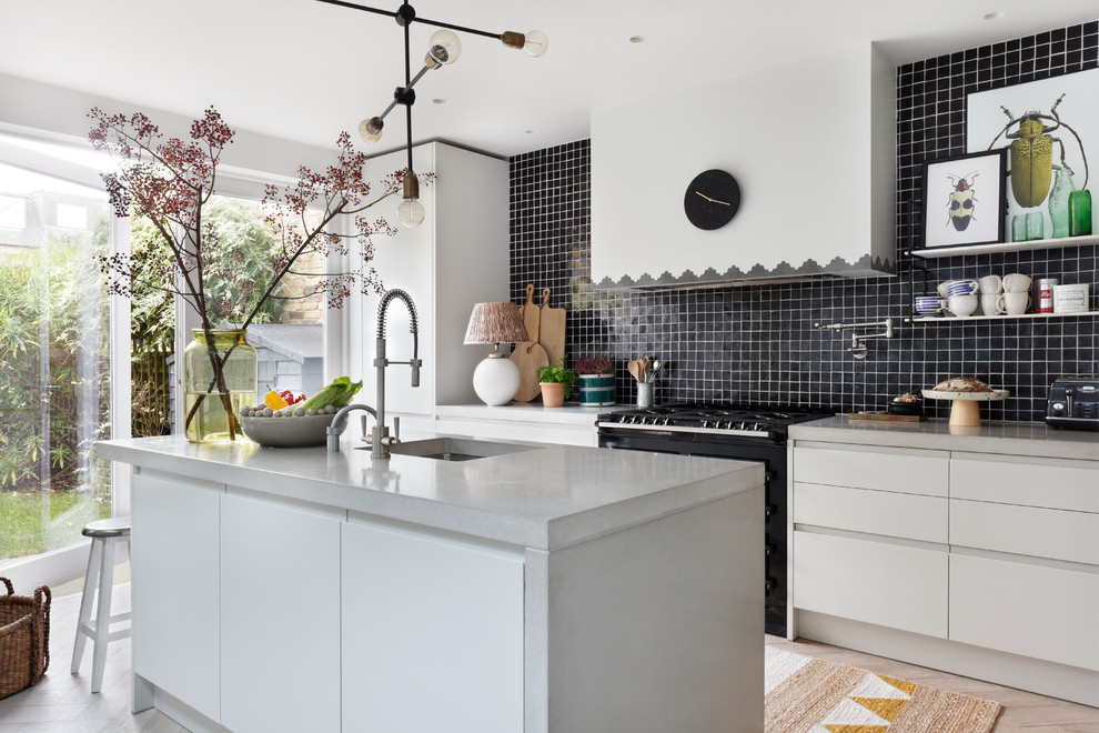Photo of a contemporary single-wall kitchen in London with an undermount sink, flat-panel cabinets, white cabinets, black splashback, black appliances, light hardwood floors, with island and concrete benchtops.