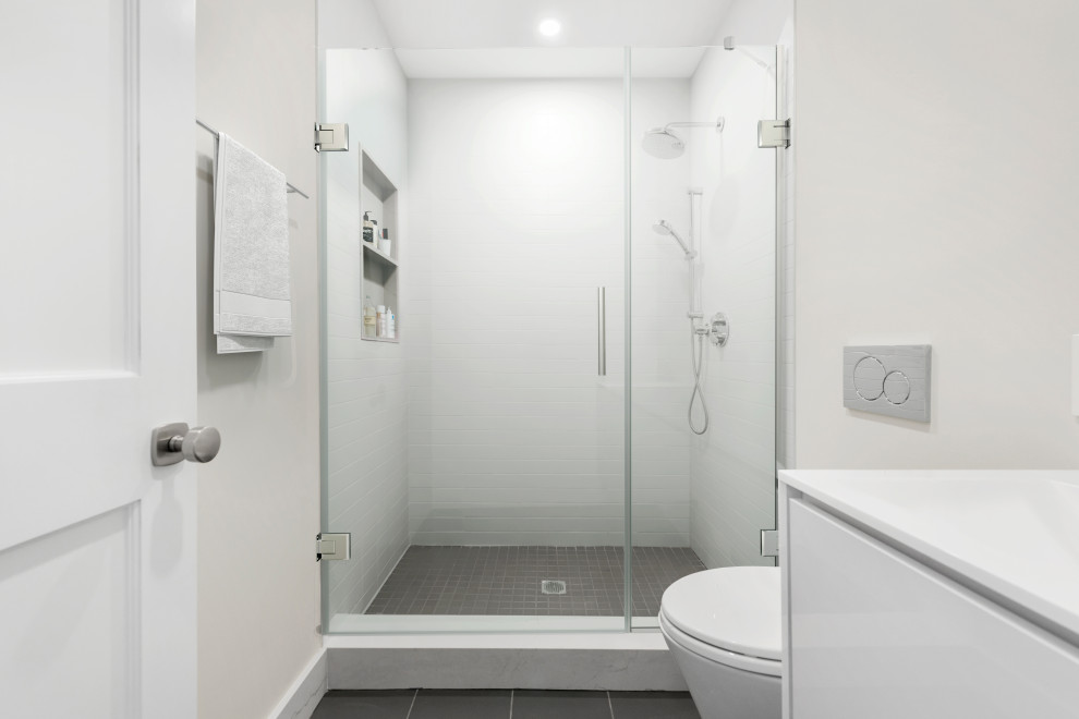 Photo of a mid-sized transitional 3/4 bathroom in New York with flat-panel cabinets, white cabinets, an alcove shower, a wall-mount toilet, white tile, ceramic tile, beige walls, cement tiles, a drop-in sink, marble benchtops, grey floor, a hinged shower door, white benchtops, a single vanity and a floating vanity.