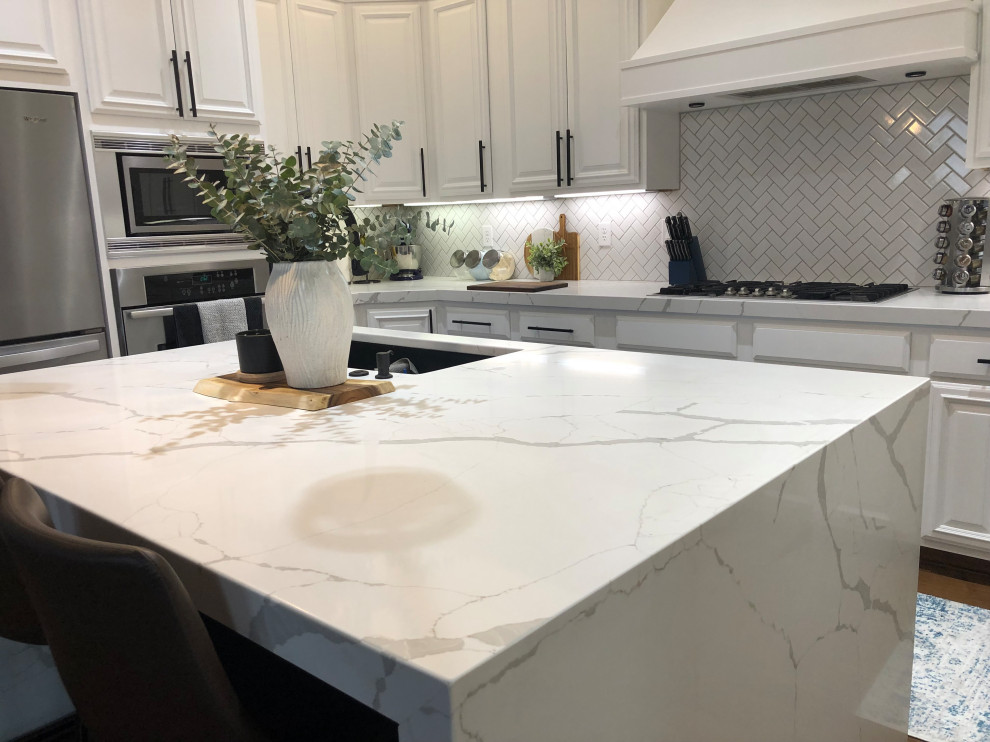 Bild på ett stort funkis vit vitt kök, med en dubbel diskho, luckor med profilerade fronter, vita skåp, bänkskiva i kvarts, vitt stänkskydd, stänkskydd i cementkakel, rostfria vitvaror, mellanmörkt trägolv, en köksö och brunt golv