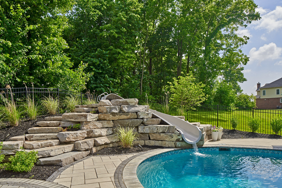 Large contemporary back custom shaped swimming pool in Detroit with a water slide and concrete paving.