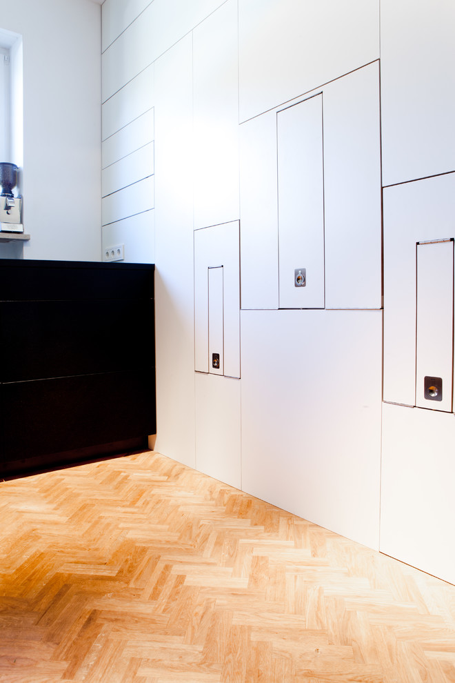 Photo of a large contemporary l-shaped open plan kitchen in Munich with flat-panel cabinets, white cabinets, medium hardwood floors, an integrated sink, solid surface benchtops, white splashback, ceramic splashback, stainless steel appliances, no island and brown floor.