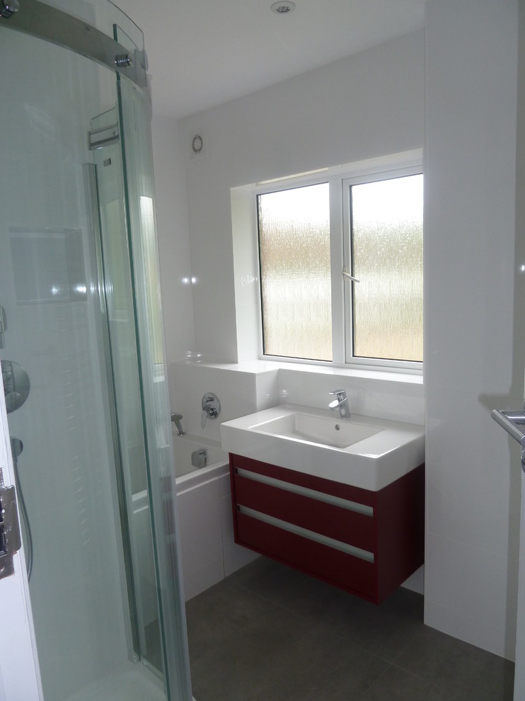 Photo of a mid-sized contemporary kids bathroom in Sussex with flat-panel cabinets, red cabinets, a drop-in tub, a corner shower, a wall-mount toilet, white tile, ceramic tile, white walls, ceramic floors and a drop-in sink.