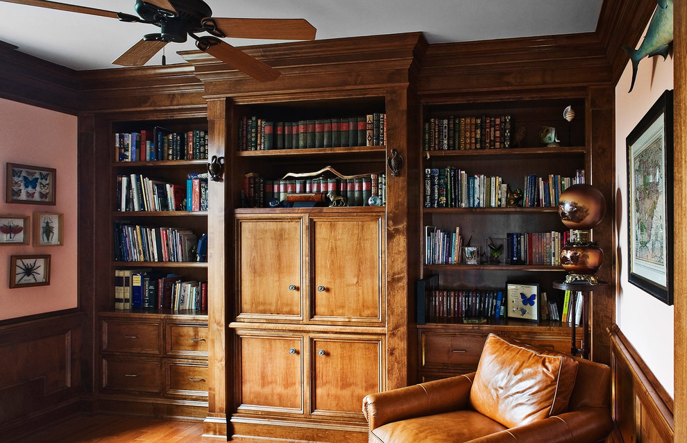 This is an example of a mid-sized country home office in New York with a library, pink walls, light hardwood floors and no fireplace.