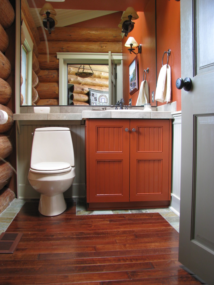 Design ideas for a mid-sized country powder room in Seattle with recessed-panel cabinets, orange cabinets, orange walls, medium hardwood floors and a two-piece toilet.