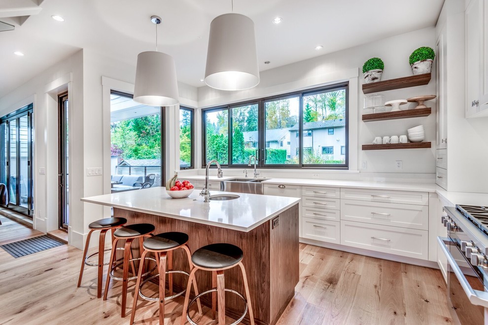 Transitional l-shaped light wood floor and beige floor kitchen photo in Vancouver with a farmhouse sink, shaker cabinets, white cabinets, stainless steel appliances, an island and white countertops