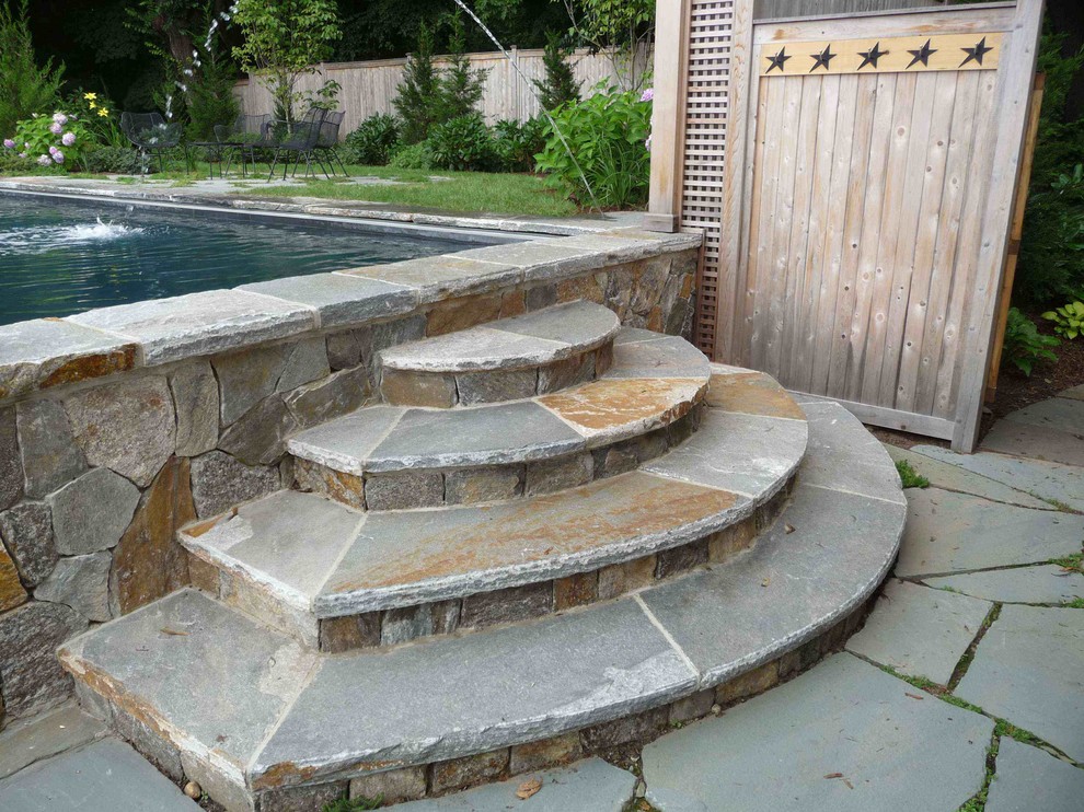 This is an example of a modern backyard rectangular infinity pool in Bridgeport with a water feature and natural stone pavers.