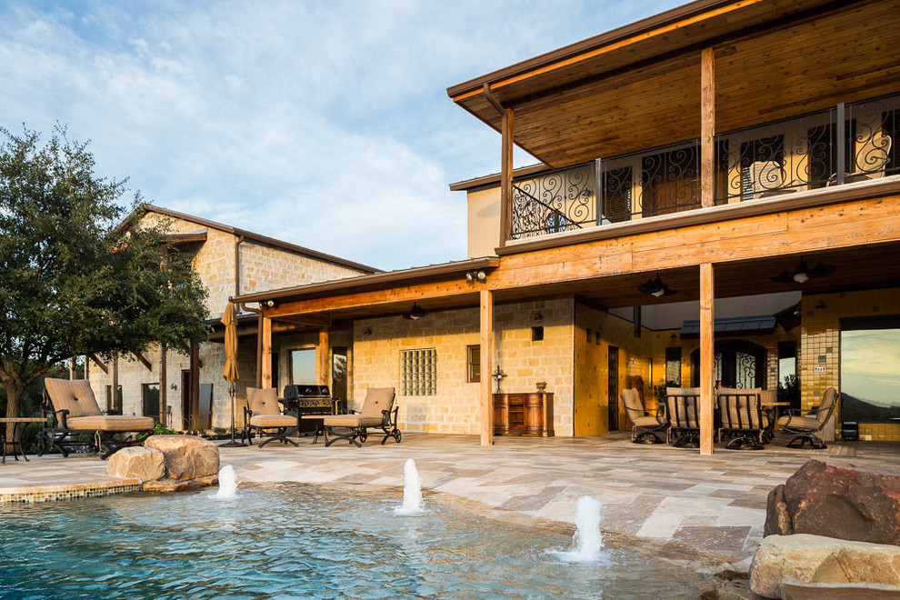 Photo of an expansive traditional backyard custom-shaped infinity pool in Austin with natural stone pavers.